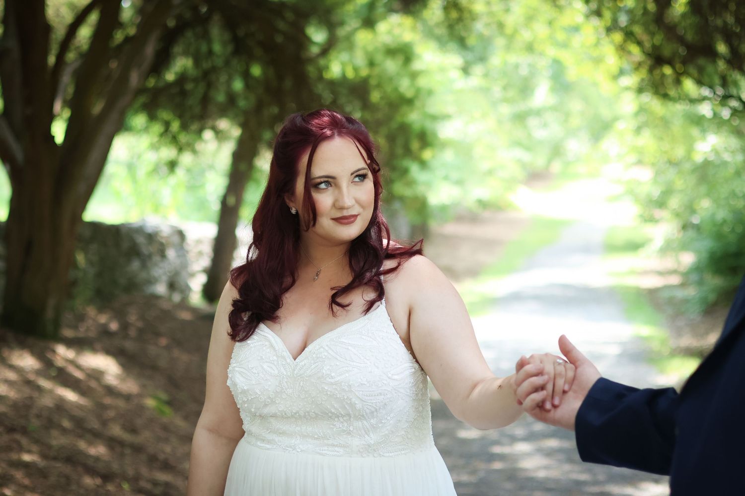 A bride and groom share a romantic moment together on a tree-lined path in a park setting.
