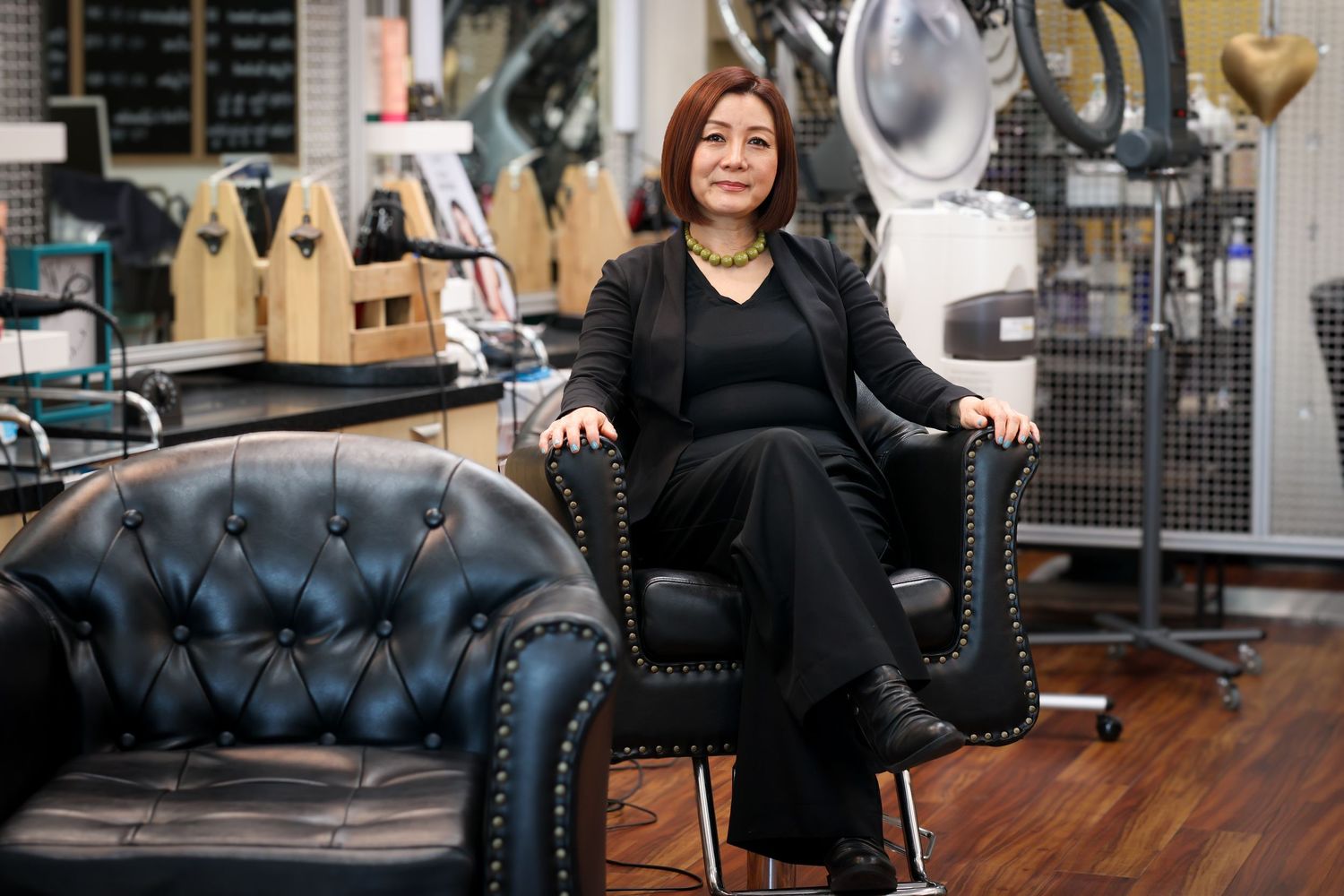 A stylish black leather tufted salon chair sits in front of a wooden floor and mirrored wall.