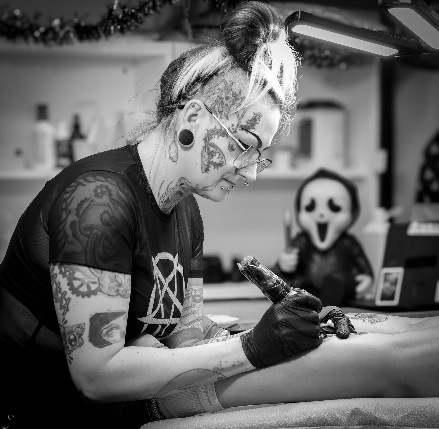 Professional tattoo artist works meticulously on a client's arm in a clean studio setting.