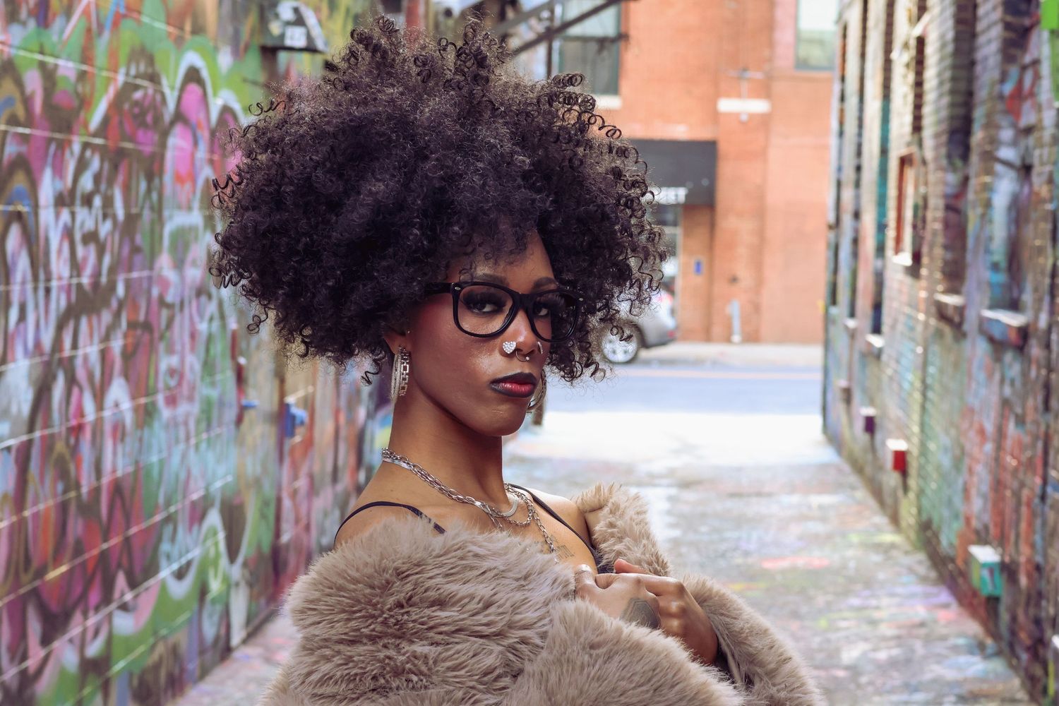 Model in fluffy coat and glasses strikes artistic poses against vibrant street art backdrop.