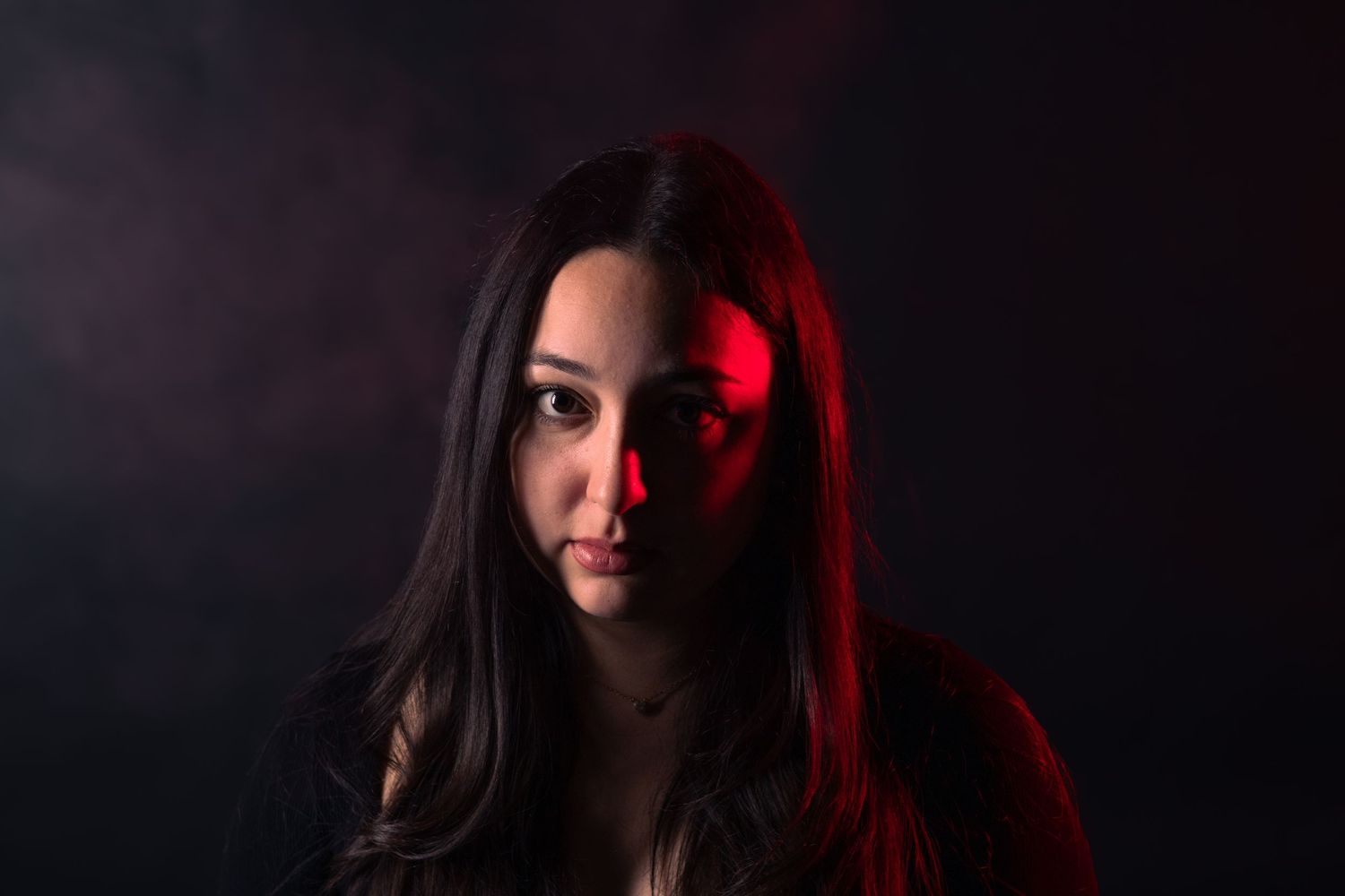 Woman with long dark hair posed against dark background with dramatic red and blue studio lighting.