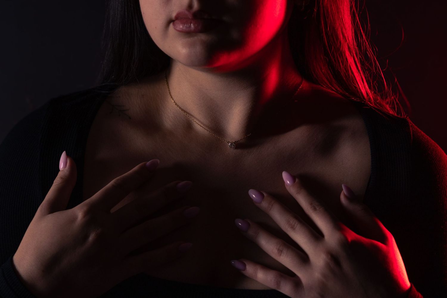 Close-up of woman's hands crossed over chest with red dramatic lighting and gold necklace.