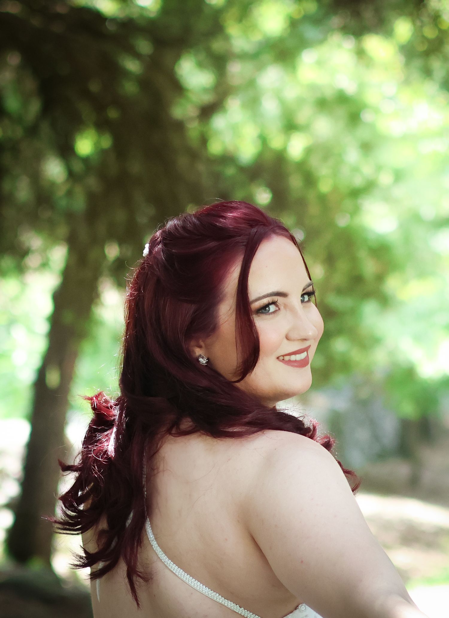 Bride in white dress poses gracefully against blurred green garden background.