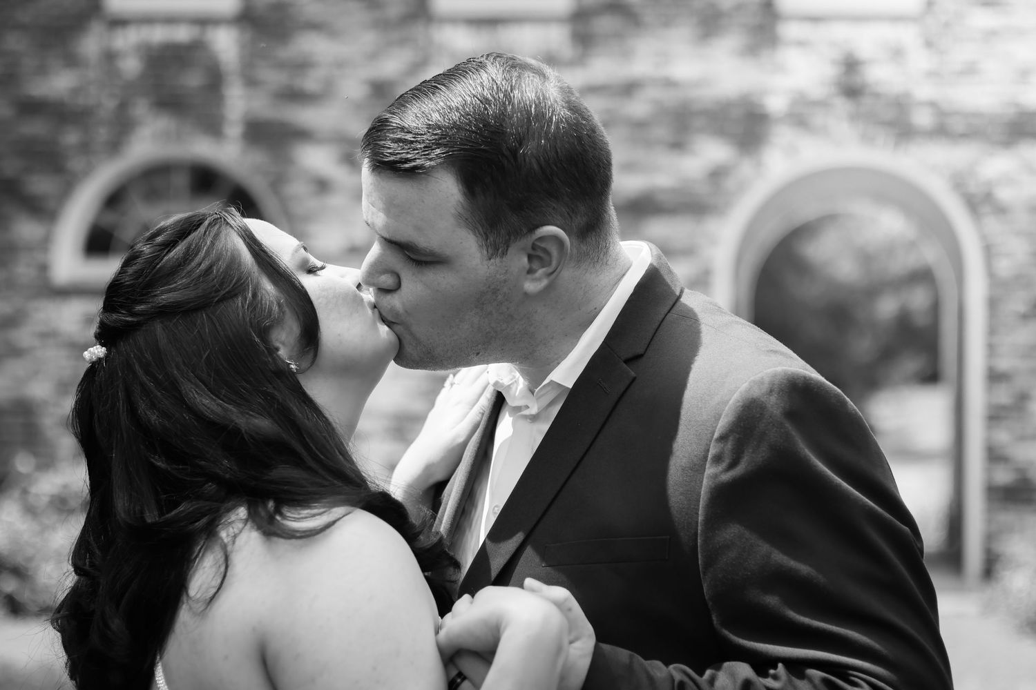 Black and white wedding portrait with couple sharing intimate moment against stone wall.