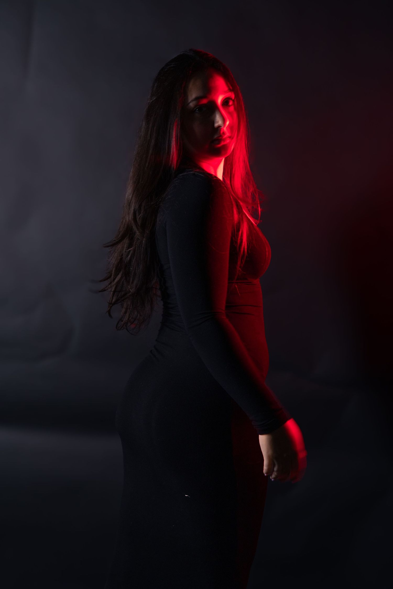 Woman in black dress posed dramatically under red lighting against dark background.