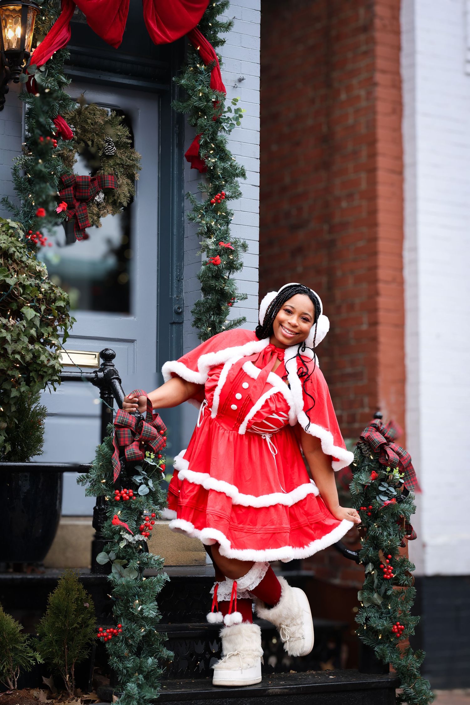 Young woman in red Mrs. Claus costume with white fur trim poses on decorated Christmas steps.