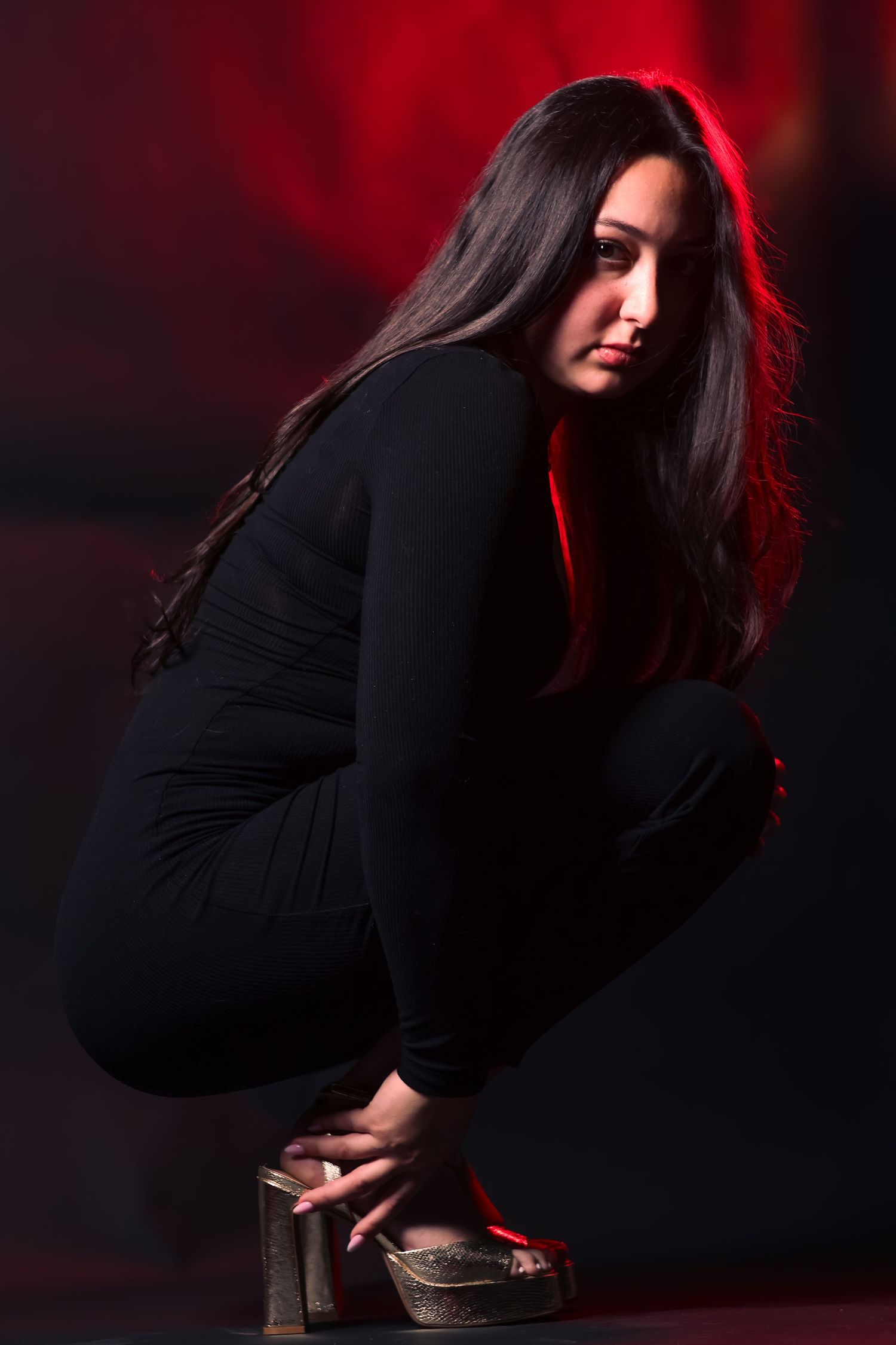 Woman in black outfit crouching dramatically against dark background with red lighting.