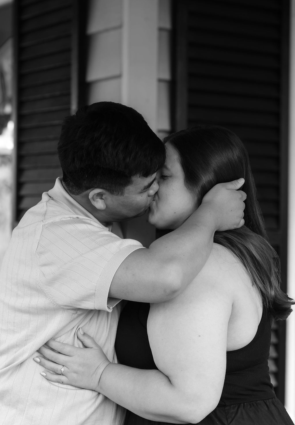 Black and white photo of a couple embracing and kissing on a porch, with the man's hand cradling the woman's head.