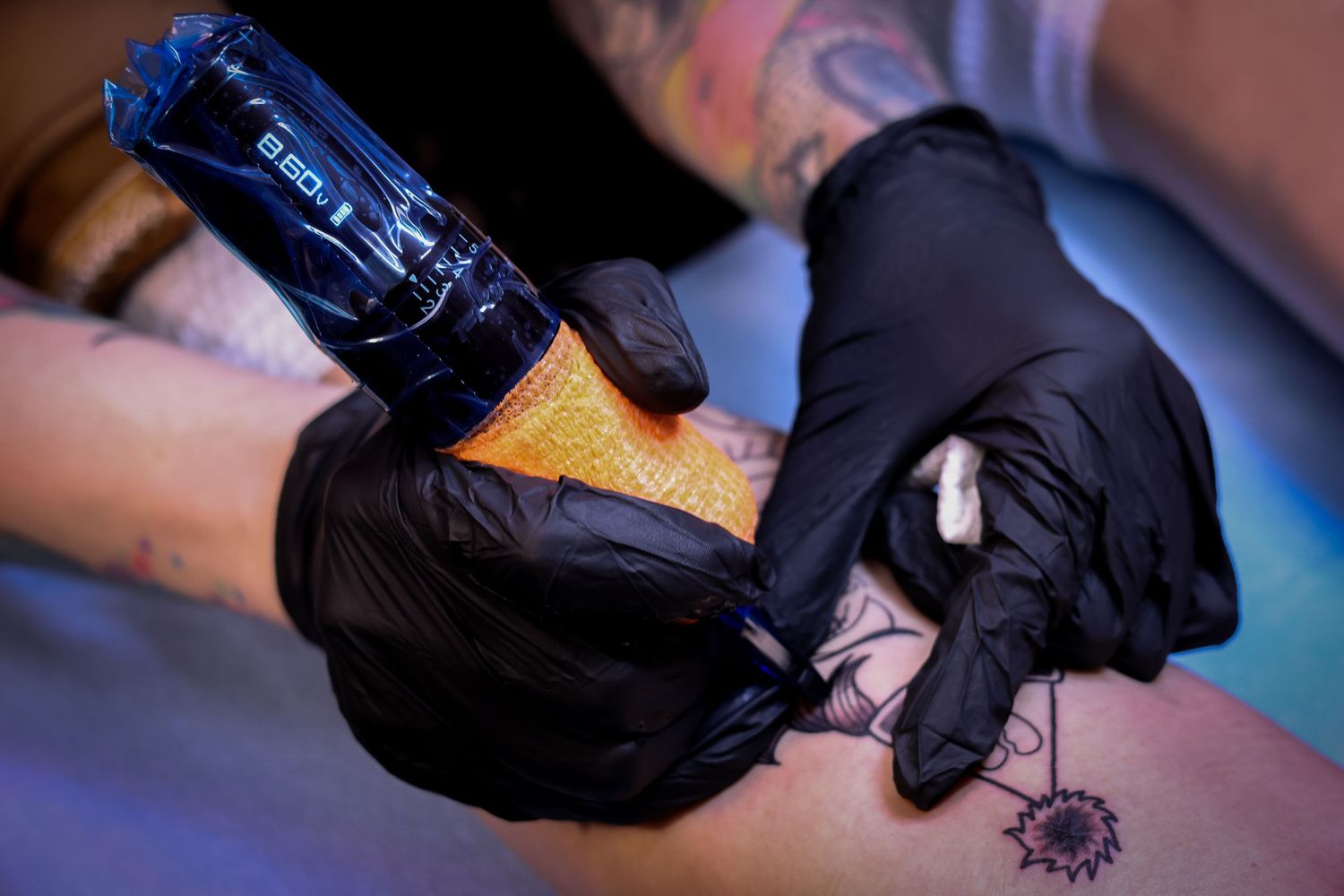 Professional tattoo artist wearing black gloves prepares equipment for a tattoo session in a studio.