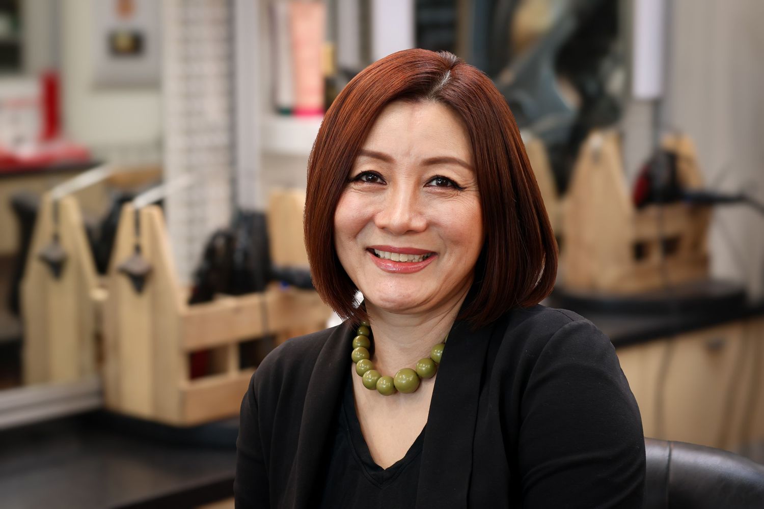 A smiling person in a black top sits in front of a light-colored background.
