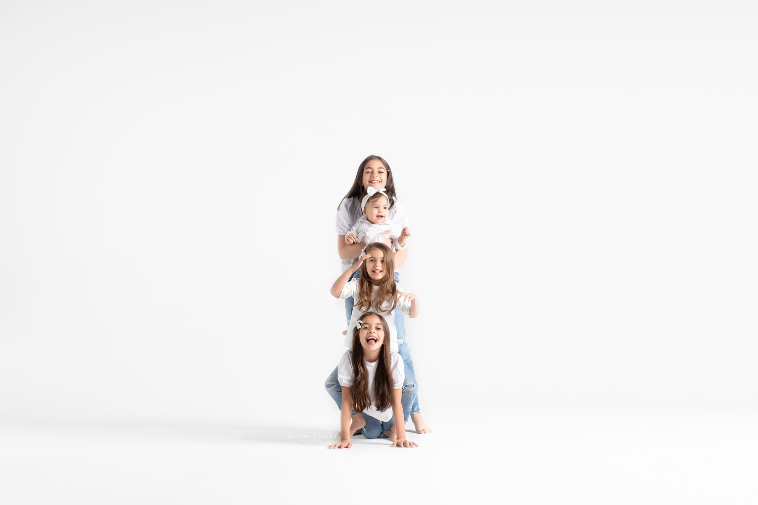 Three people playfully stacked on top of each other wearing white outfits against a light background.