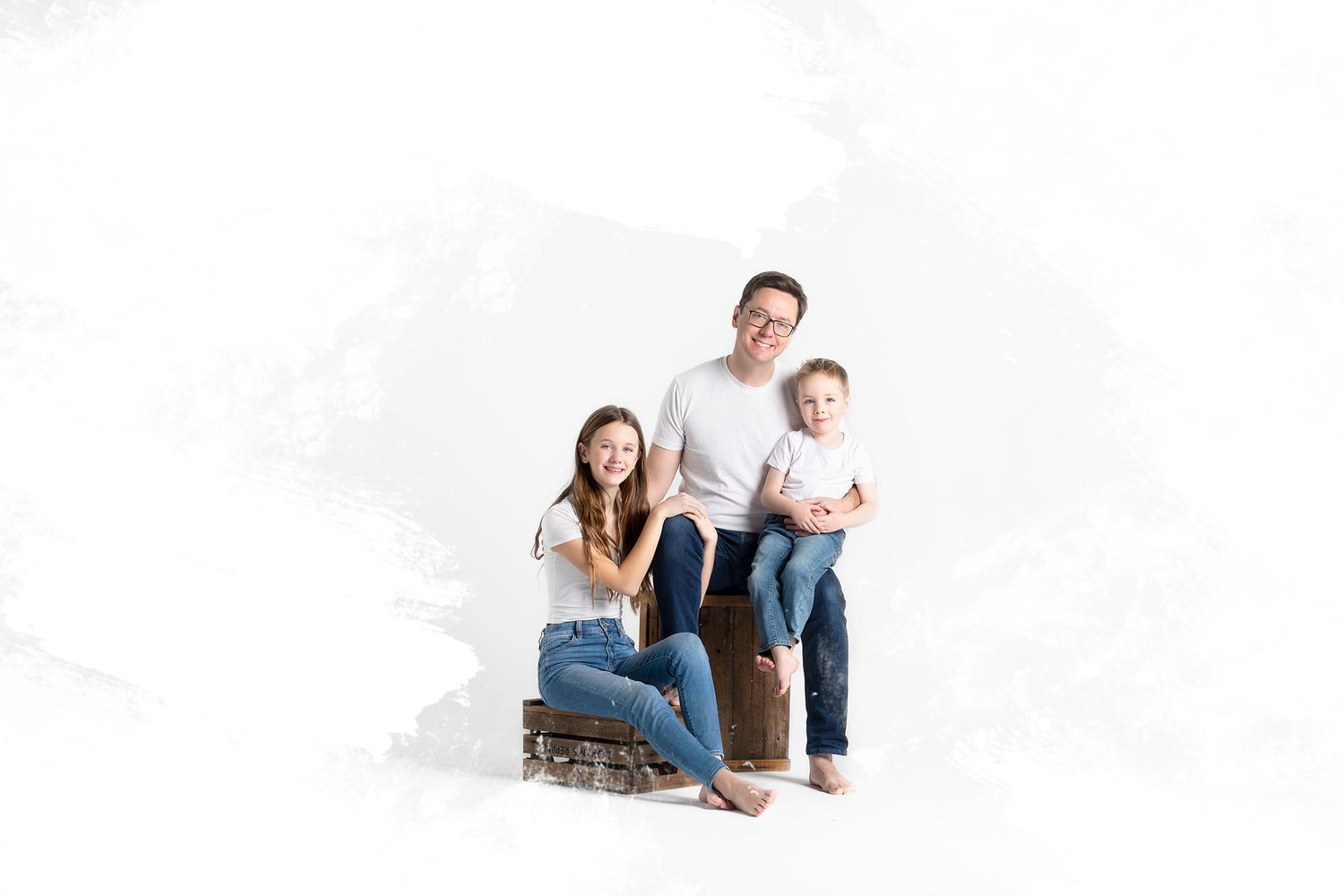 Family group sits together for casual portrait photo against white backdrop.