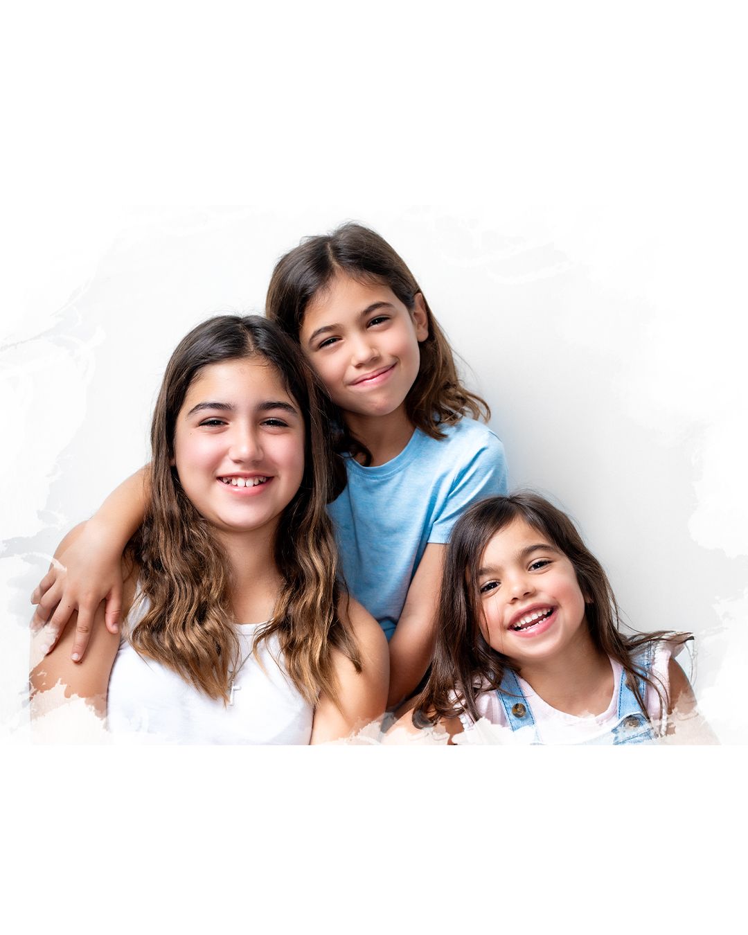 Children in white clothes sit close together while smiling and posing for a group photo.