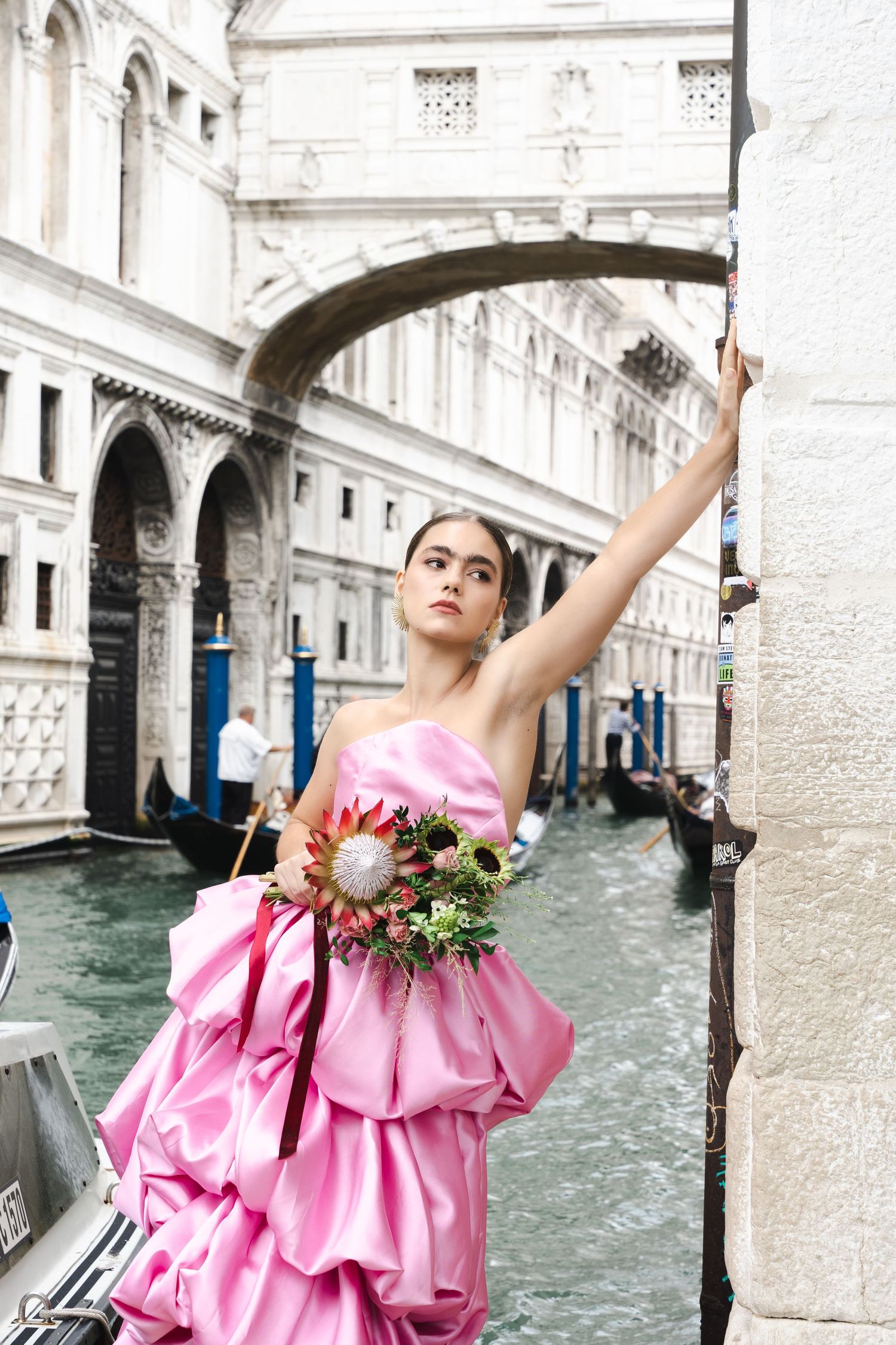 Model in pink ballgown poses with flowers under Venice's Bridge of Sighs.