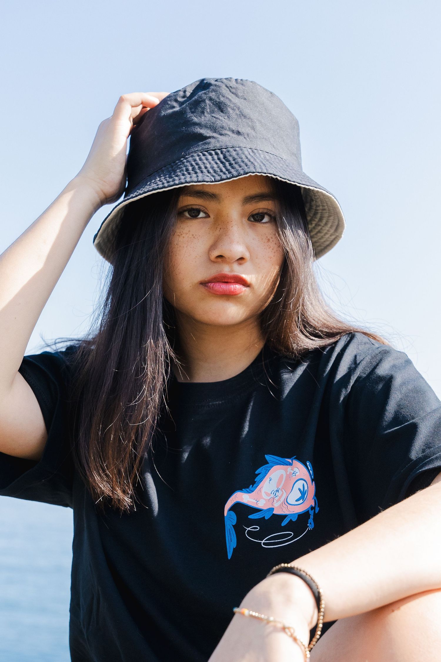 Person adjusting black bucket hat while wearing graphic t-shirt outdoors.