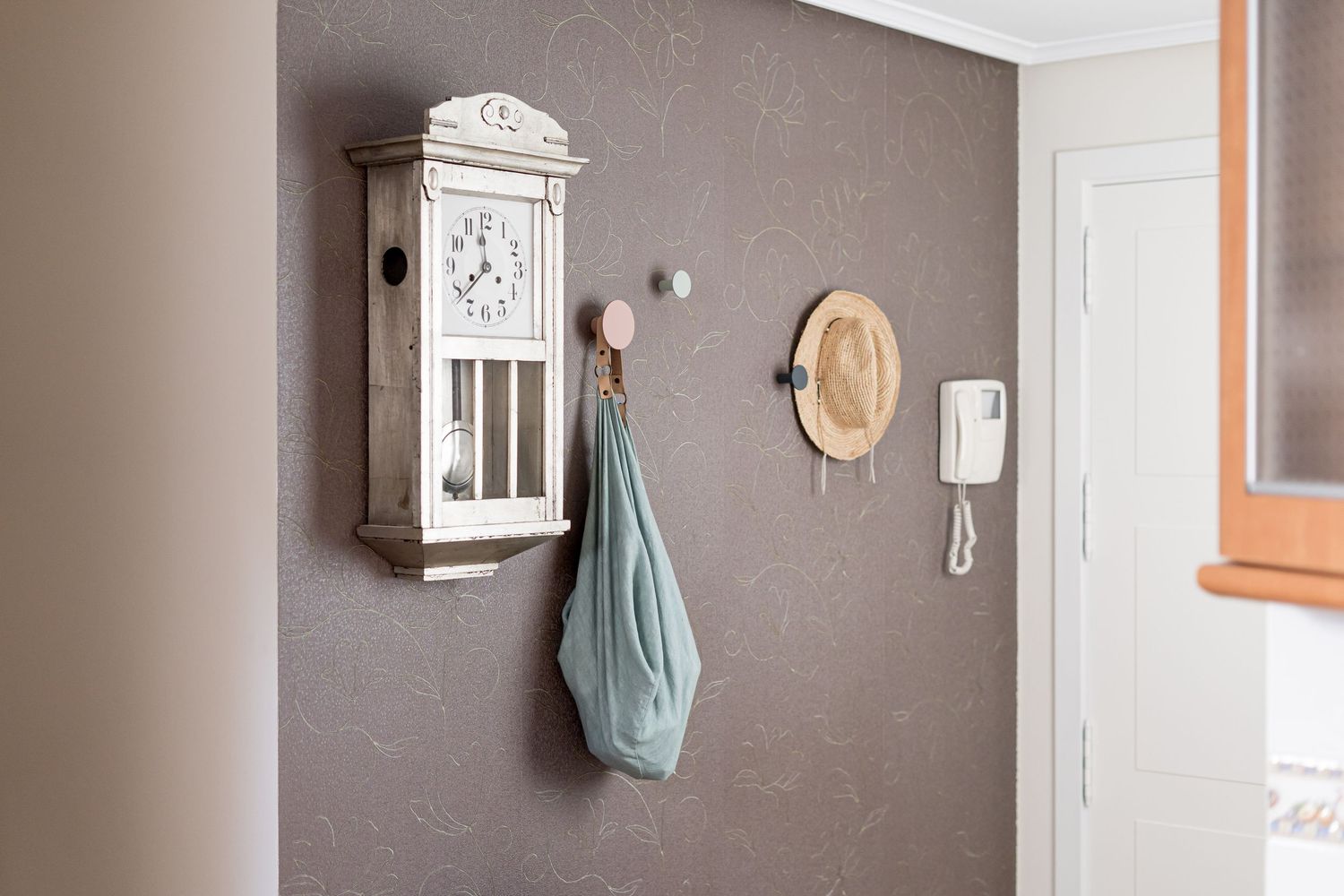 Rustic entryway wall with vintage clock, hooks, and hanging accessories.