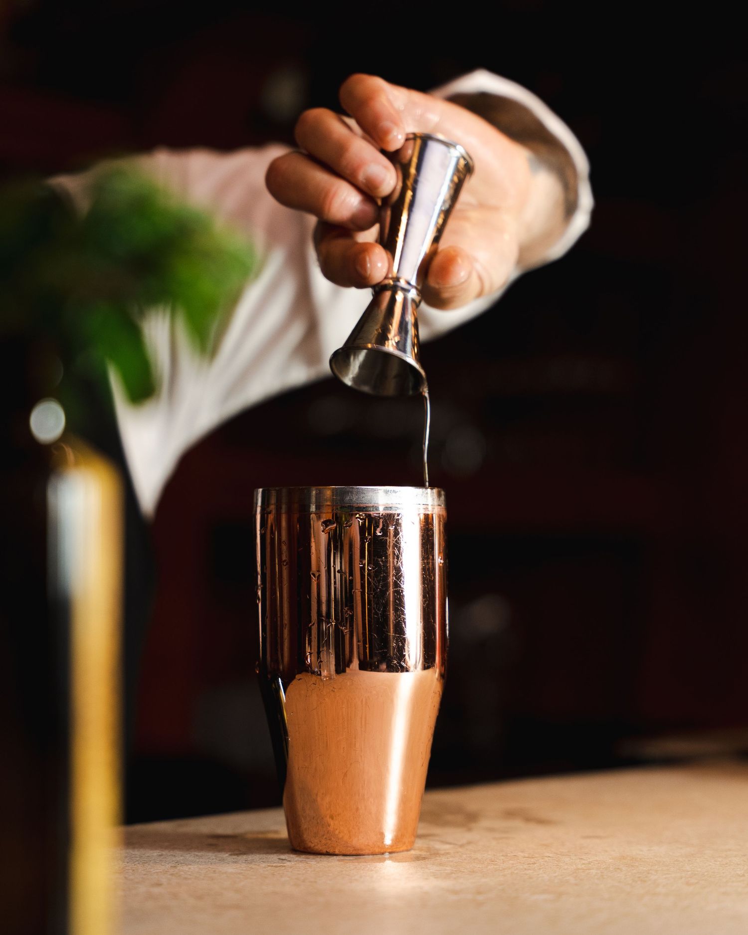 Bartender pouring liquid into a copper cocktail shaker for drink preparation.