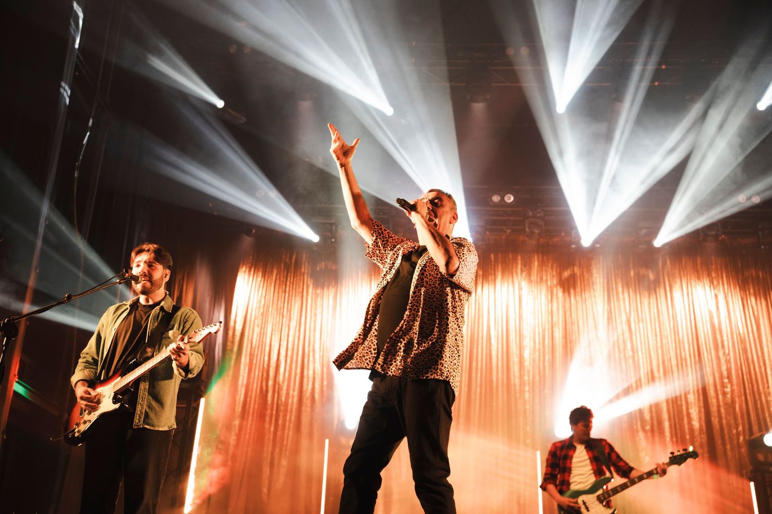 Energetic band performance with lead singer and guitarists under bright stage lighting.