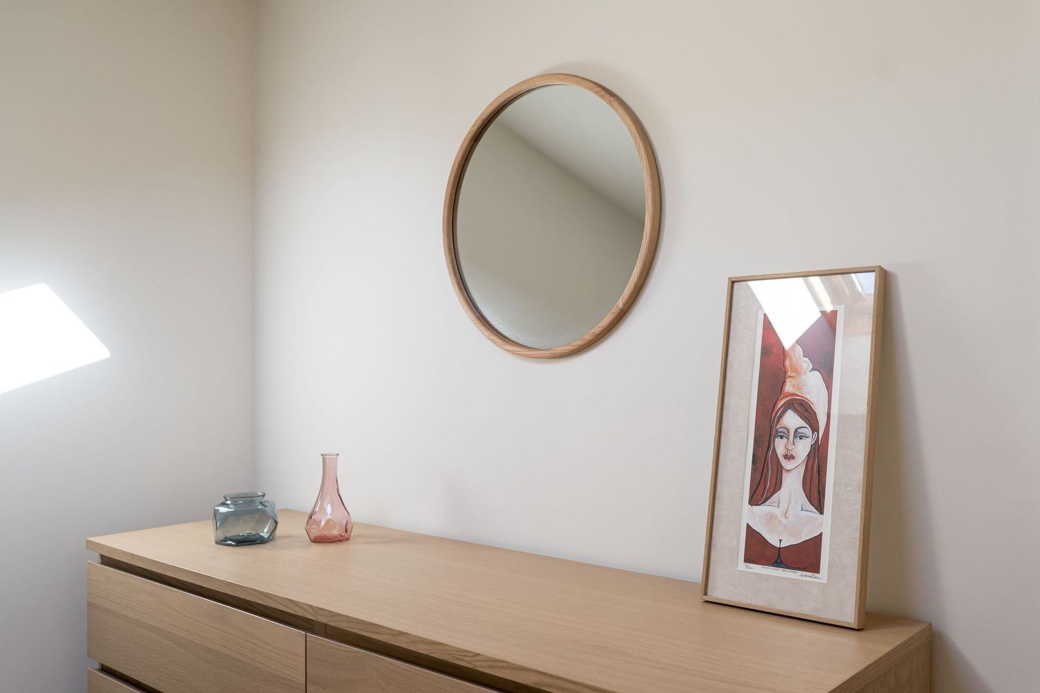 Minimalist dresser topped with round mirror and art print in neutral tones.