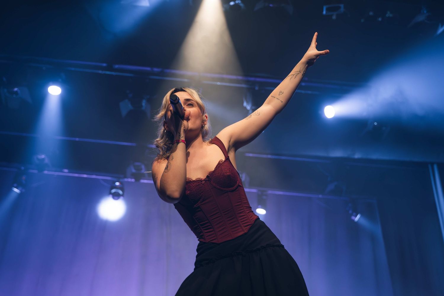 Singer performing passionately on stage with dramatic blue lighting and raised arm.