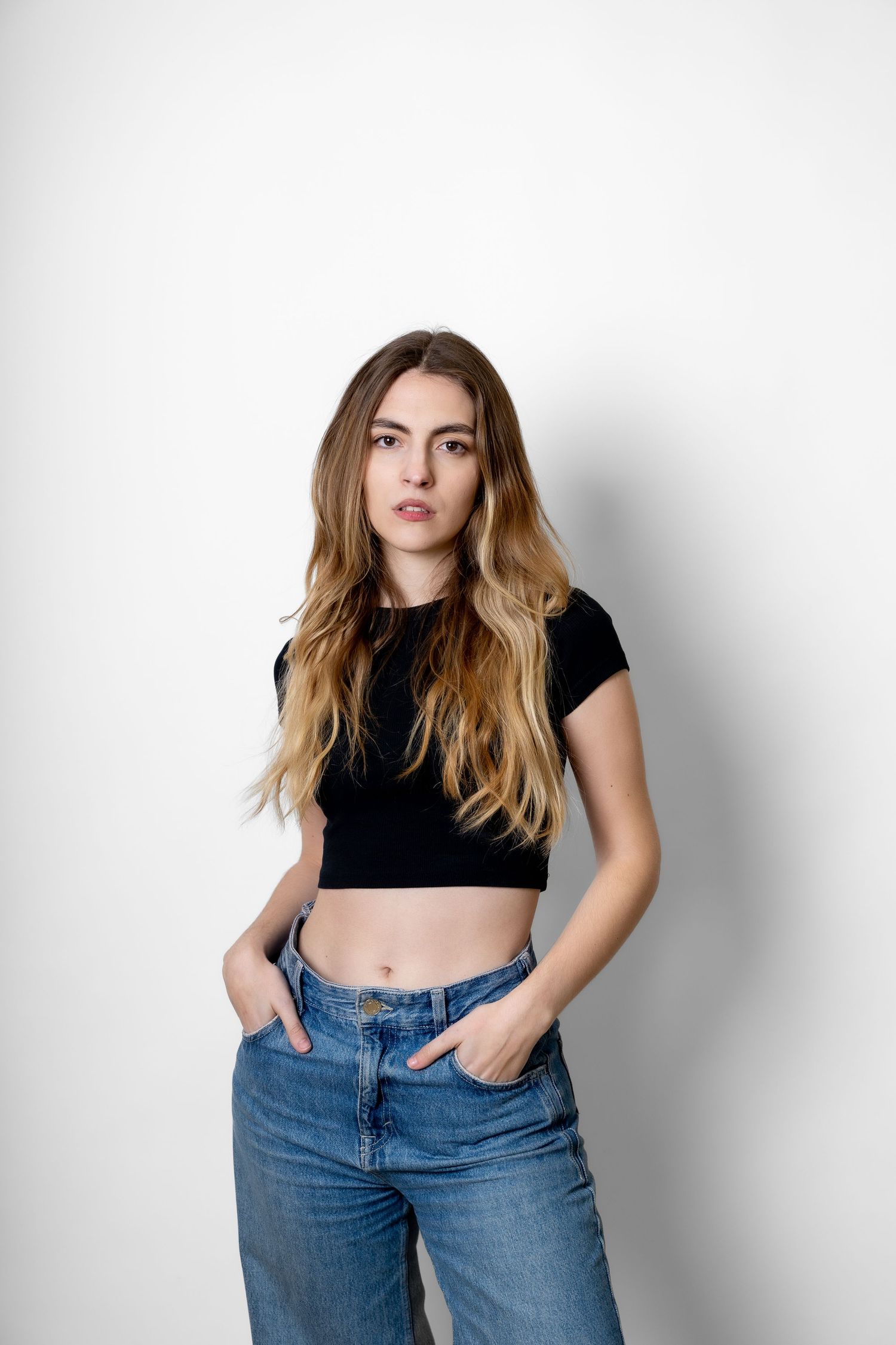 Casual fashion portrait featuring black crop top and blue denim jeans against white background.