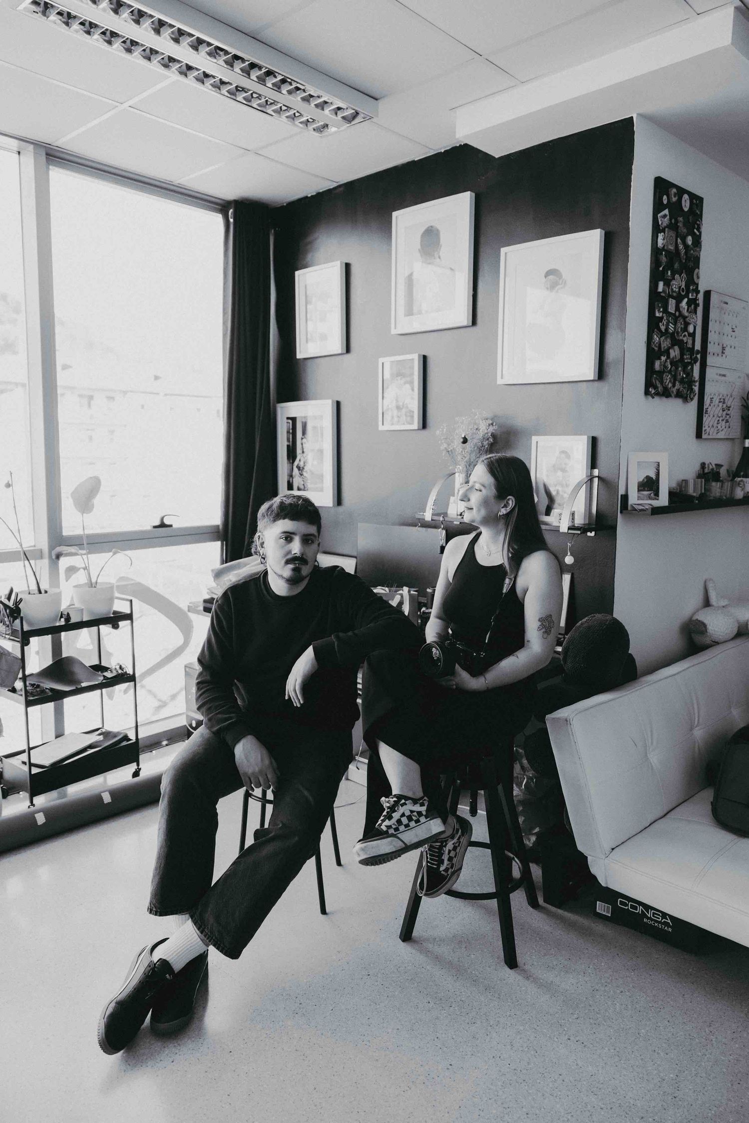 Candid black and white portrait of couple relaxing in modern studio space with artwork.