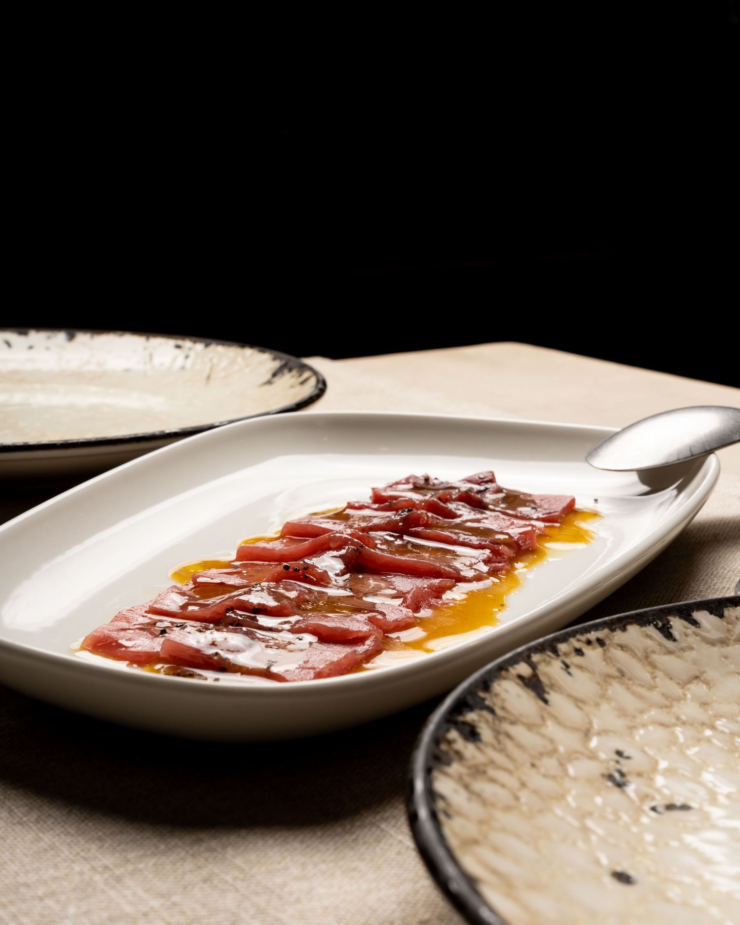 Thinly sliced cured meat arranged elegantly on a white plate with drizzled oil.