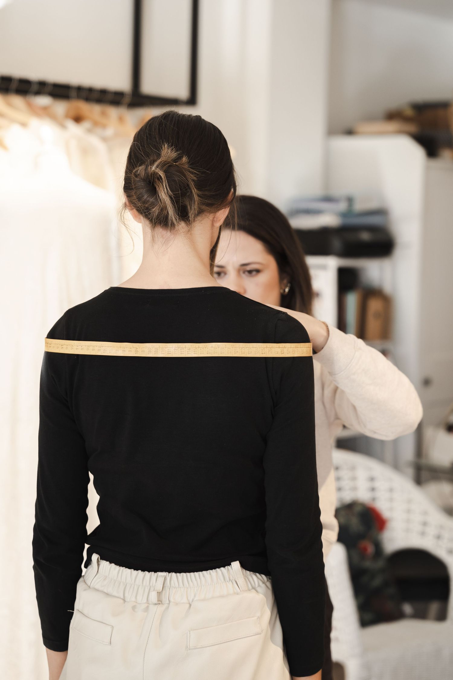 Behind the scenes fashion fitting showing black sweater with yellow measuring tape.