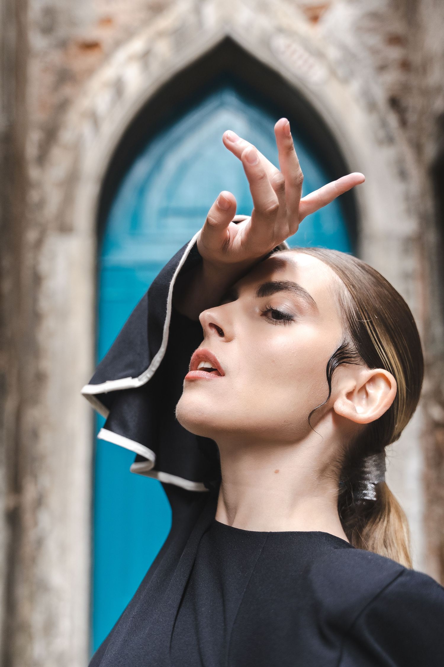 Artistic fashion portrait with model gesturing against blue gothic doorway.