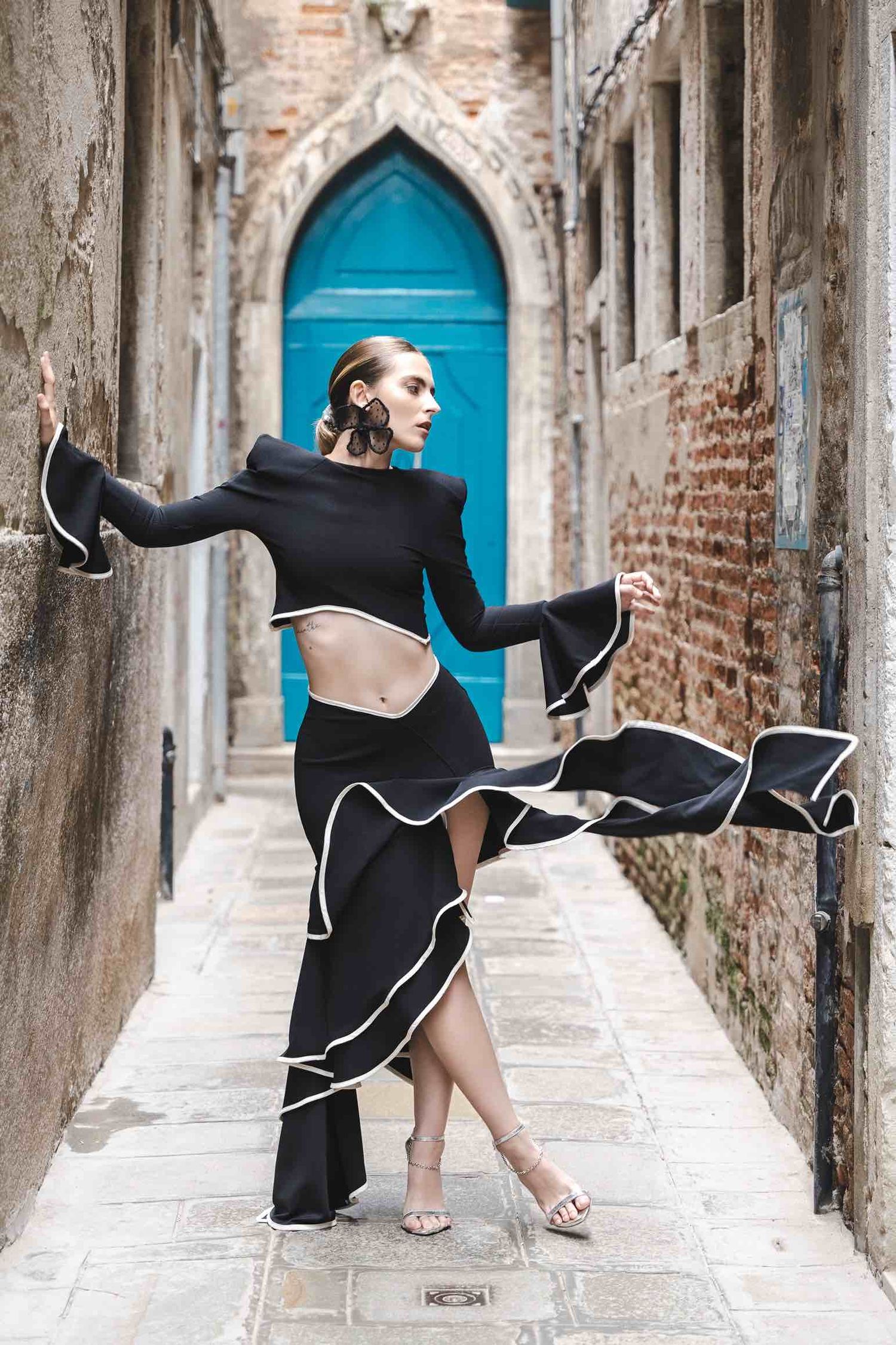 Dancer in flowing black dress performs graceful movement in narrow Venetian alley with blue door.