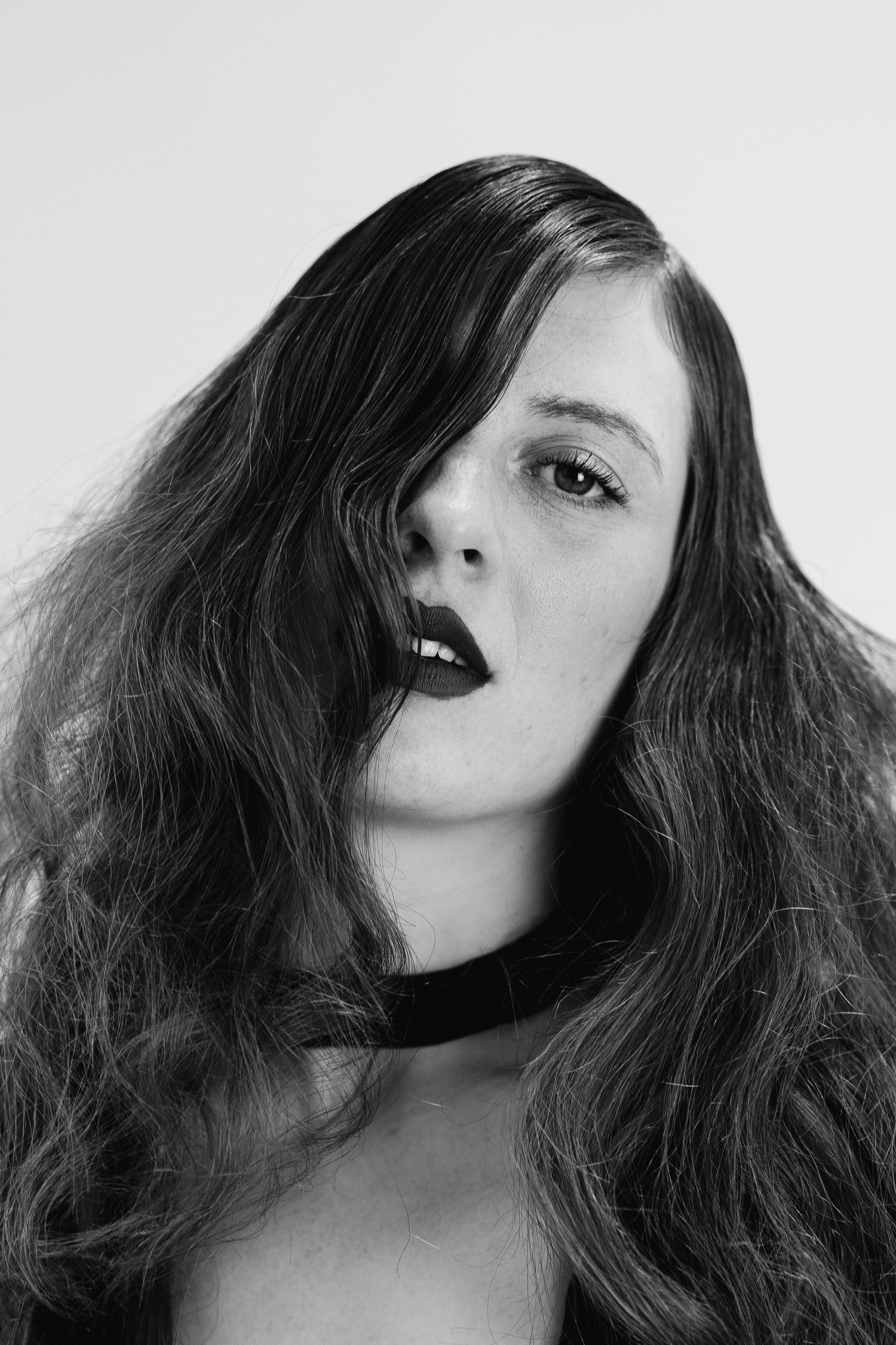 Dramatic black and white portrait of person with long dark hair and bold lipstick.