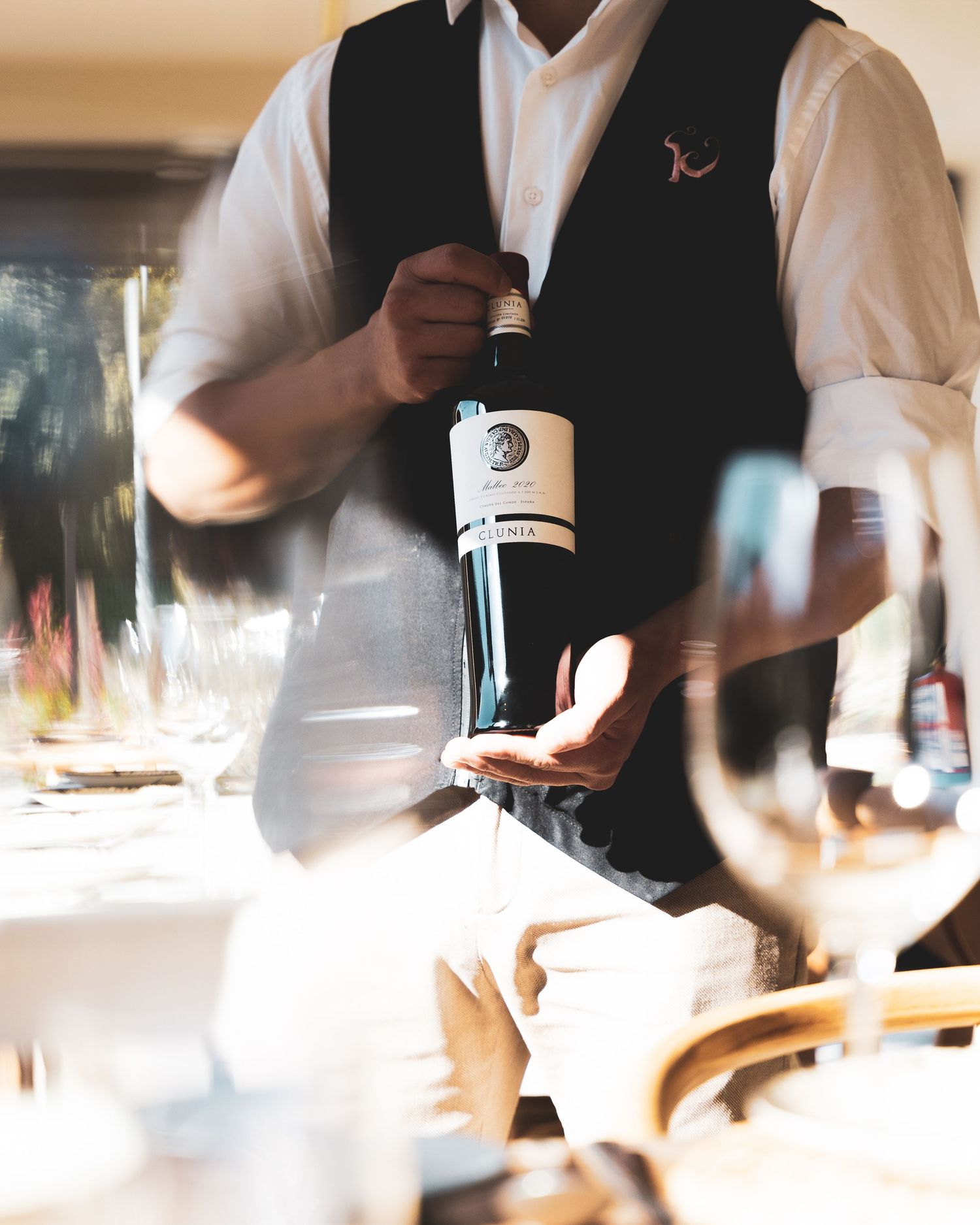 A server in formal attire pours wine from a bottle at an elegant dining setting.