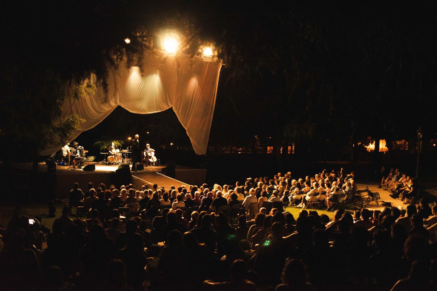 Outdoor concert venue at night with illuminated stage and large crowd.