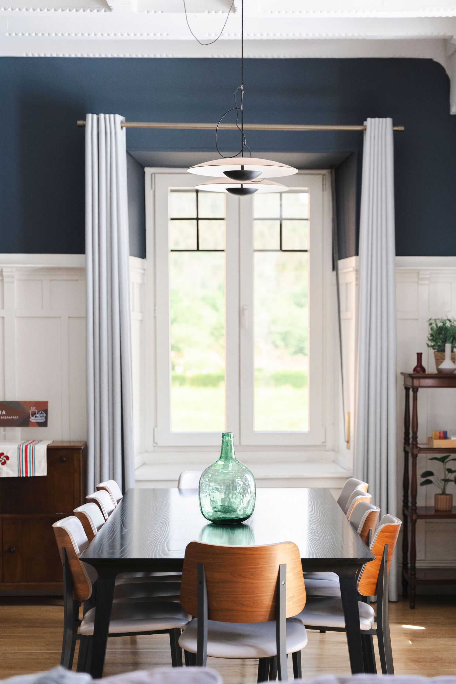 Modern dining room with navy walls, white curtains, and mid-century furniture.