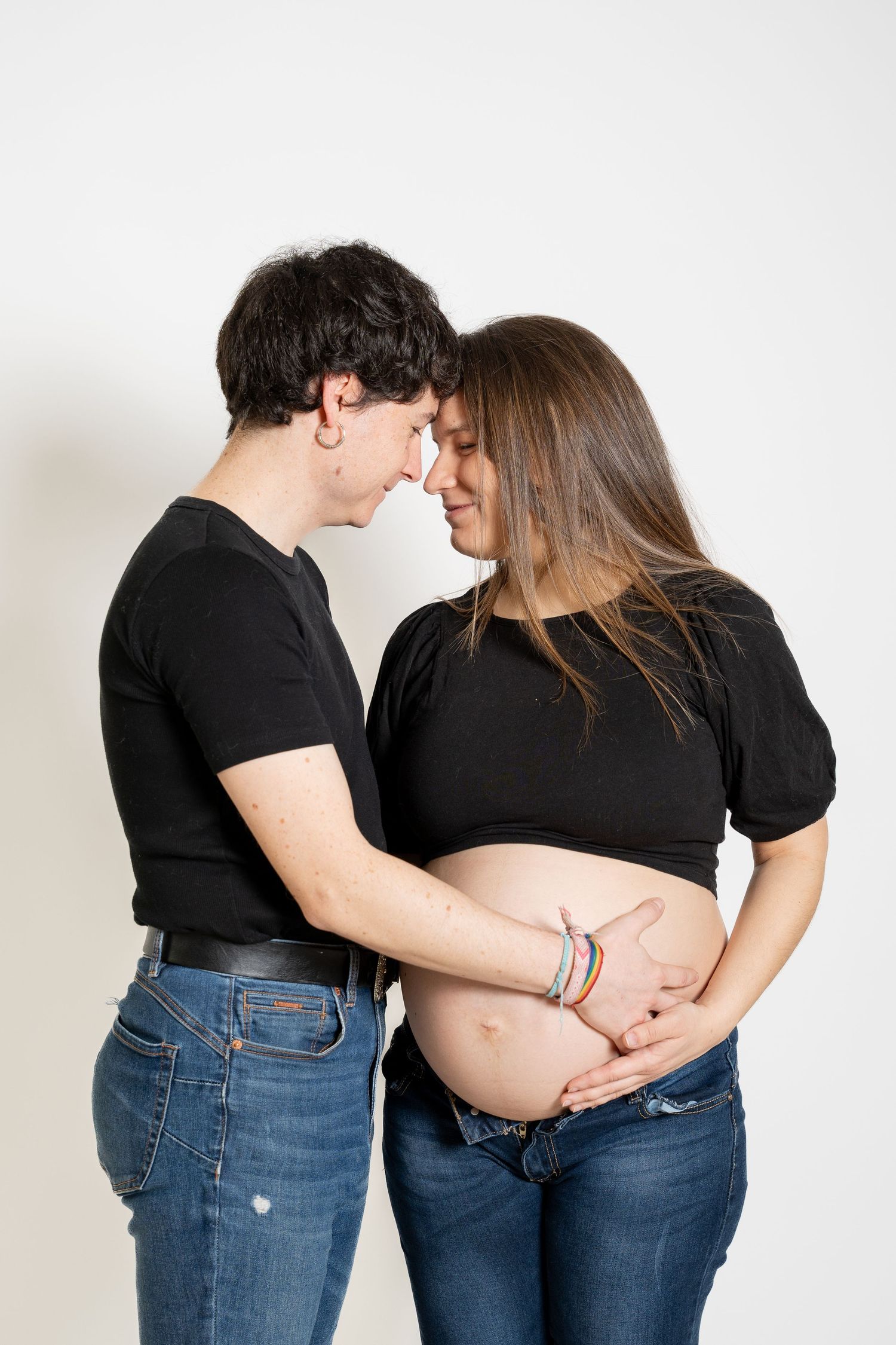Intimate maternity photo with couple in black tops touching foreheads.