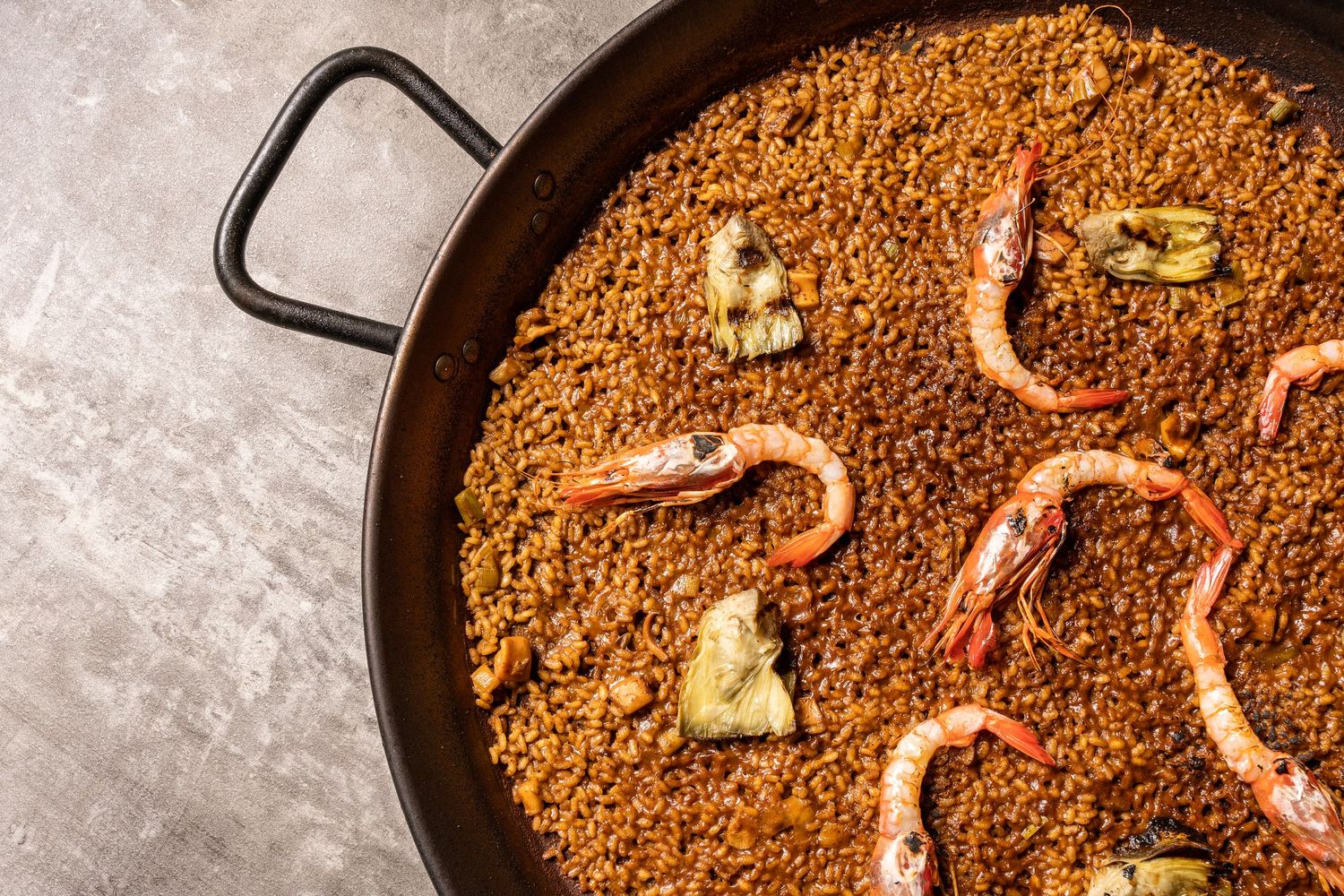 Close-up shot of sizzling paella in a traditional black pan with seafood and yellow saffron rice.