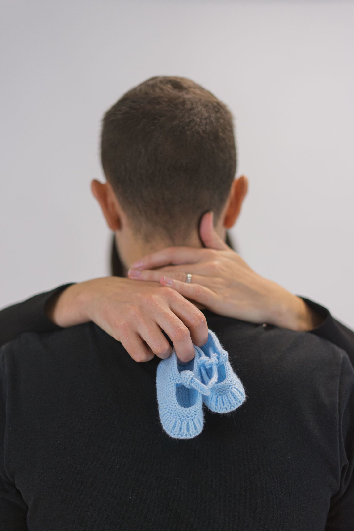 Person holding small blue baby booties while touching their neck.