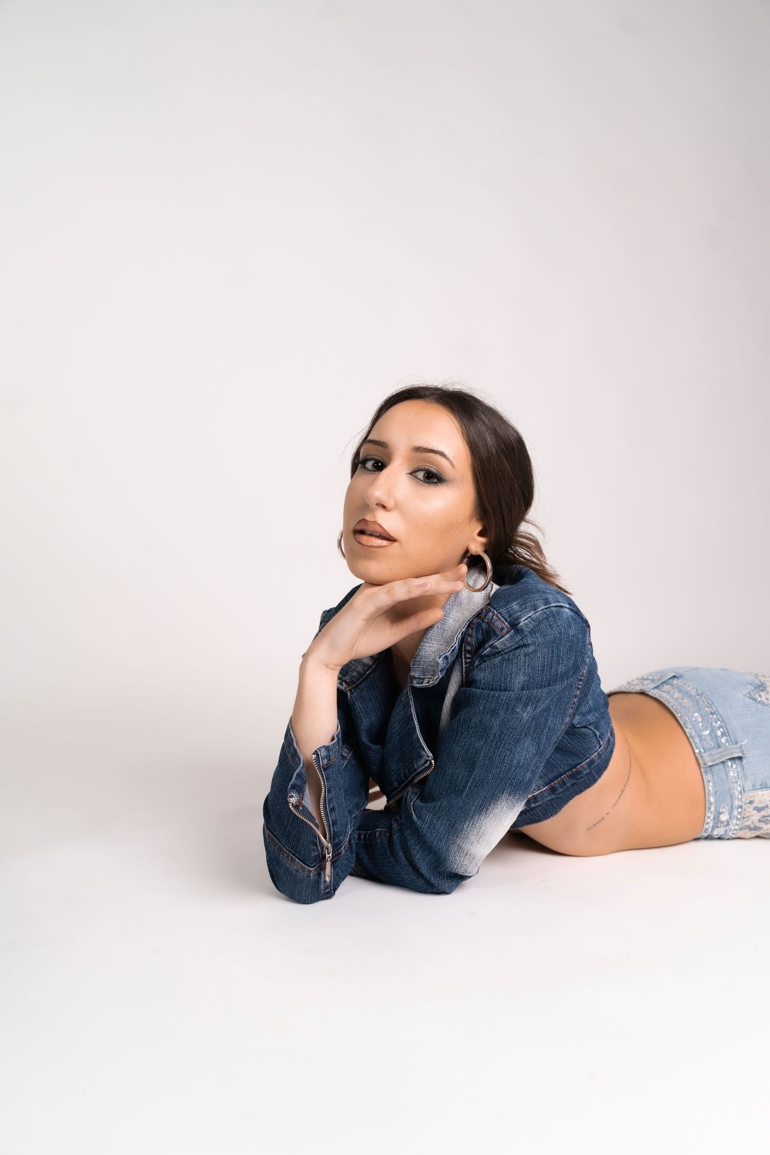 Fashion model in denim jacket poses lying down on white background.