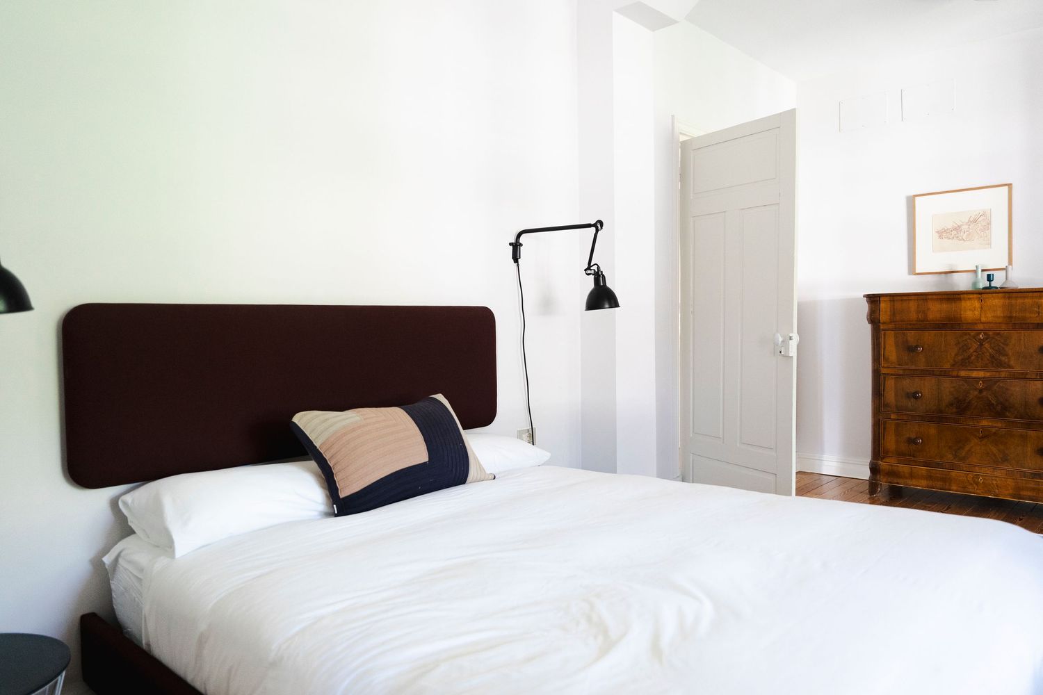 Modern bedroom with dark headboard, white bedding, and vintage wooden dresser.
