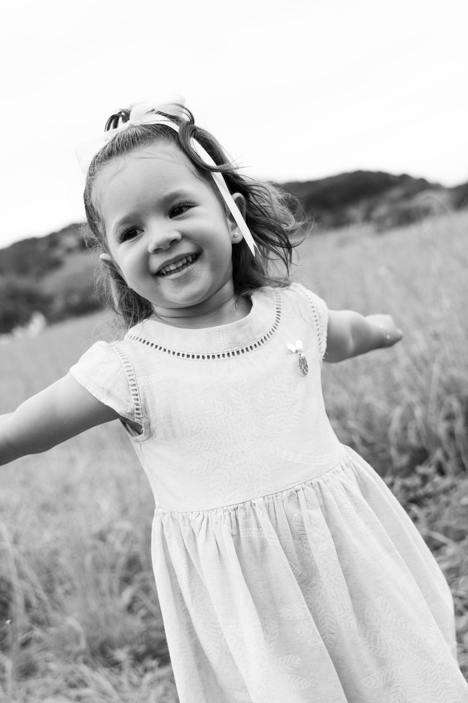 A joyful child in a white dress playing outdoors in a field.