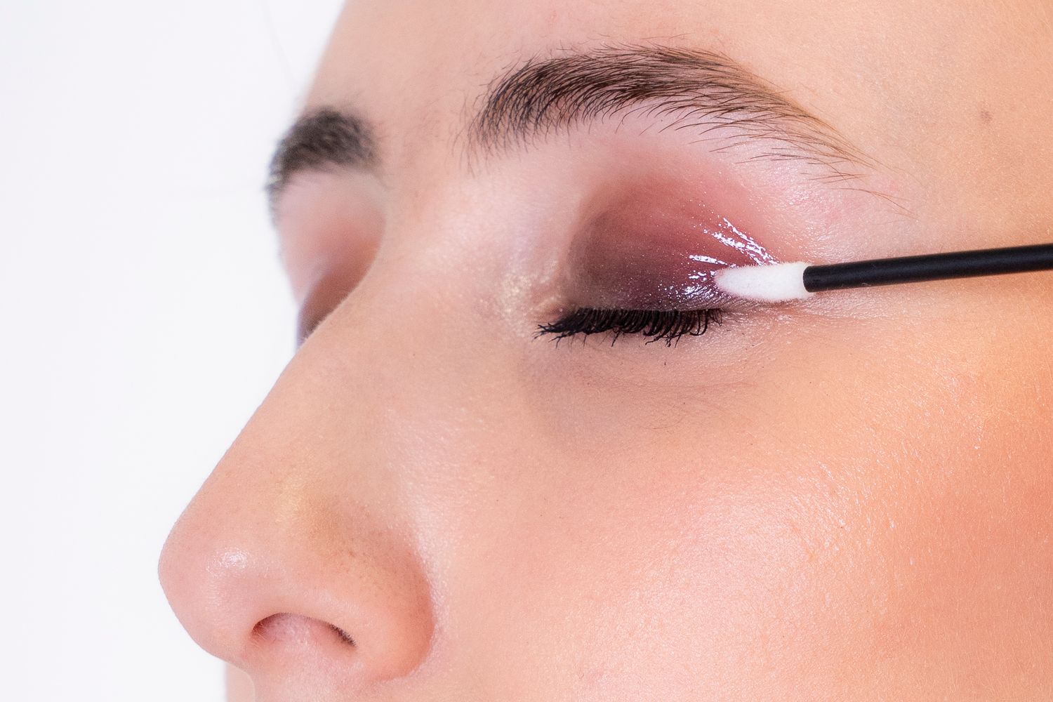 Close-up of eye makeup application using small brush with pink eyeshadow.