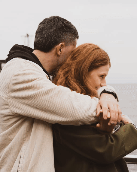 Couple embraces intimately against cloudy backdrop in candid romantic moment.