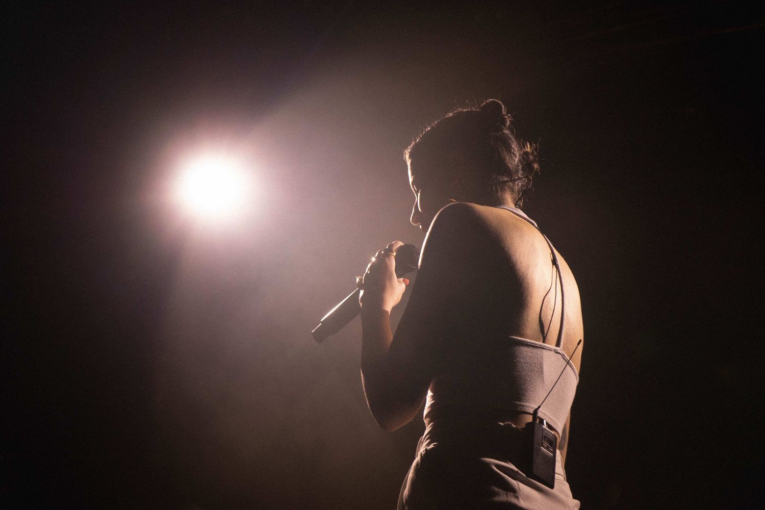 Silhouette of performer singing into microphone with dramatic backlighting.