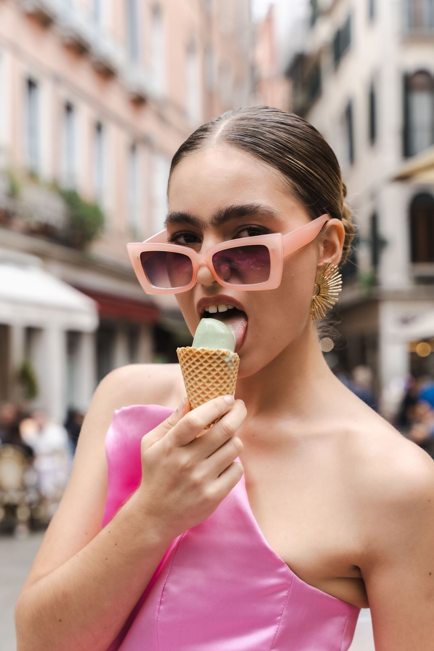 Stylish model in pink dress enjoying gelato while wearing oversized sunglasses.