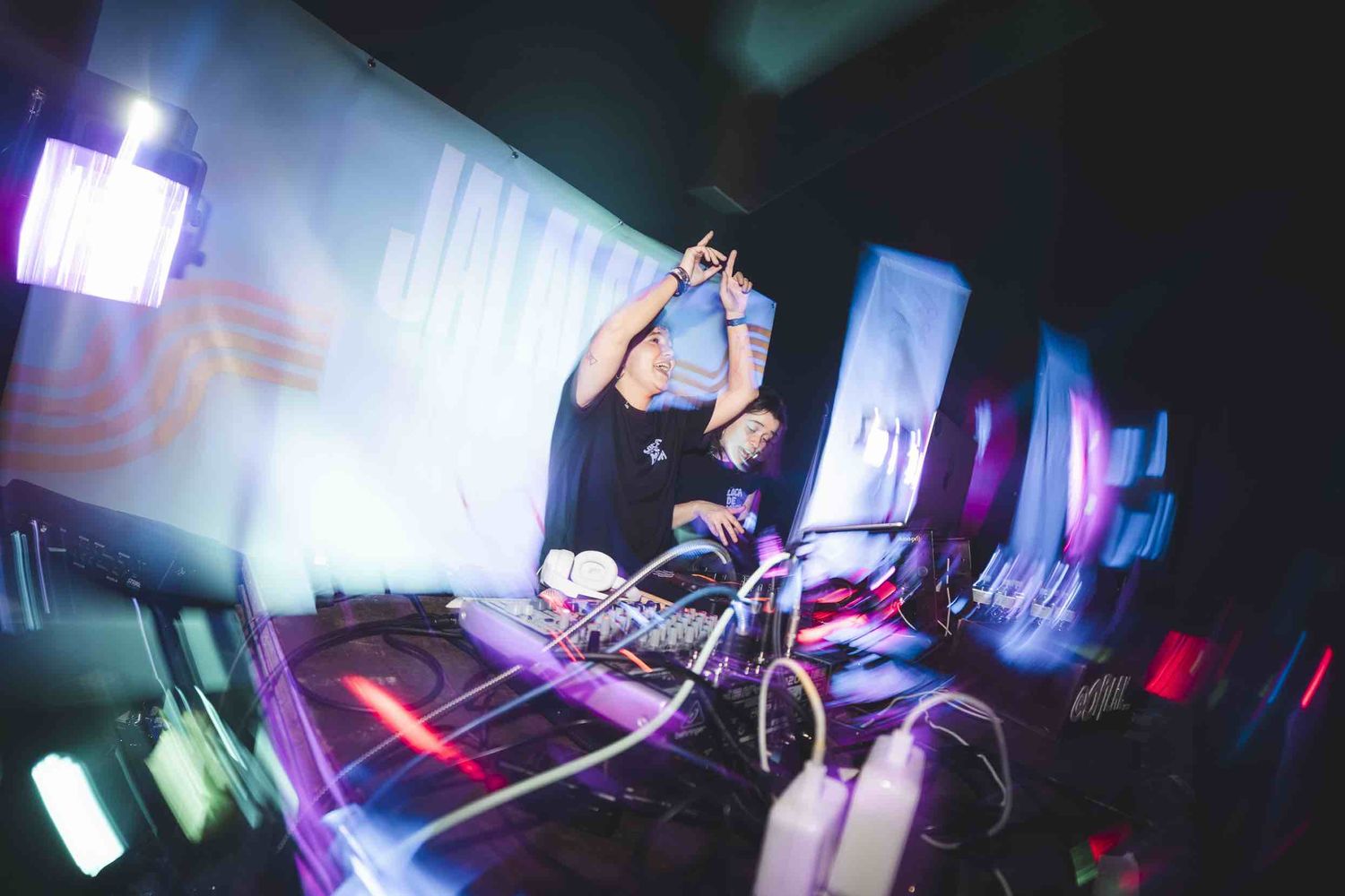DJ performing at electronic music event with colorful stage lighting and equipment.