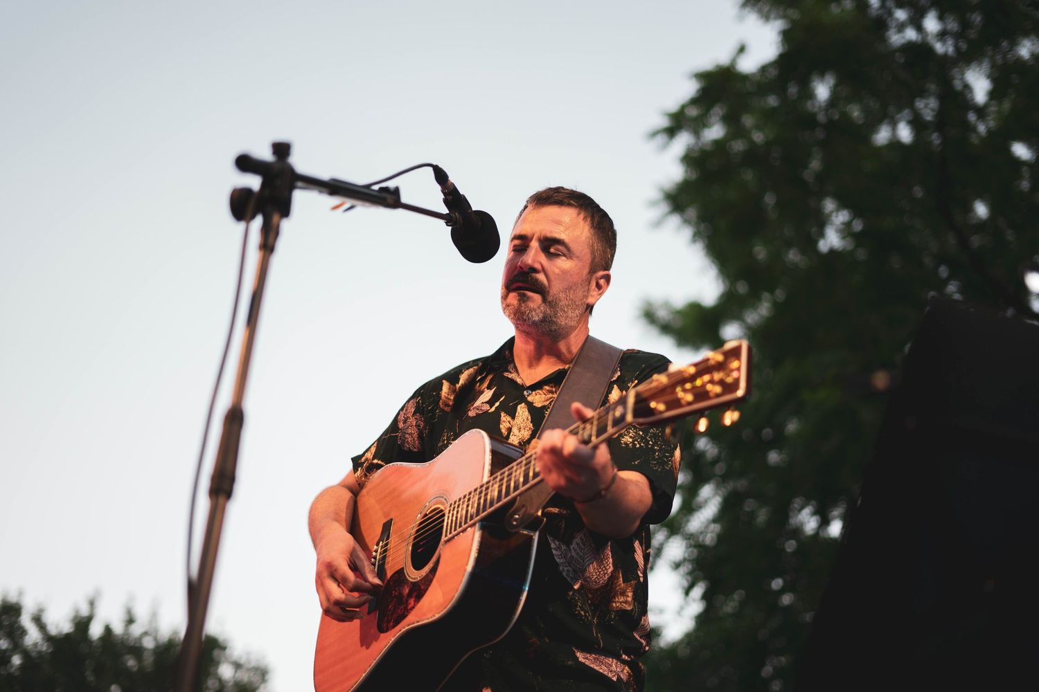 Acoustic guitarist performs outdoors at sunset with microphone setup.