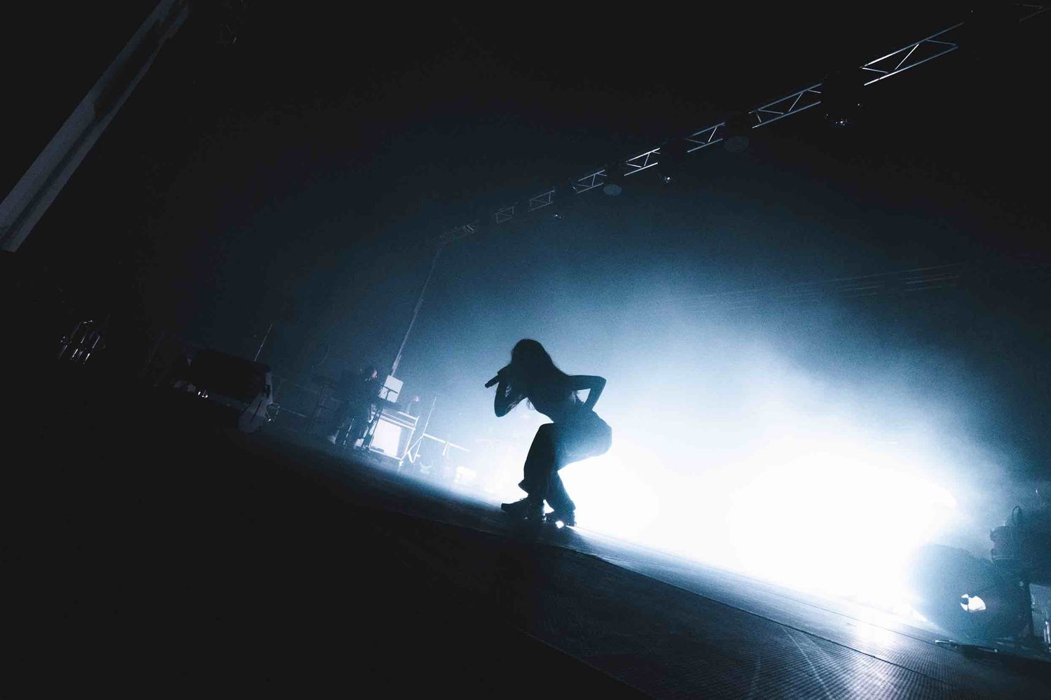 Silhouetted figure performing on stage with dramatic backlighting creating a moody atmosphere.