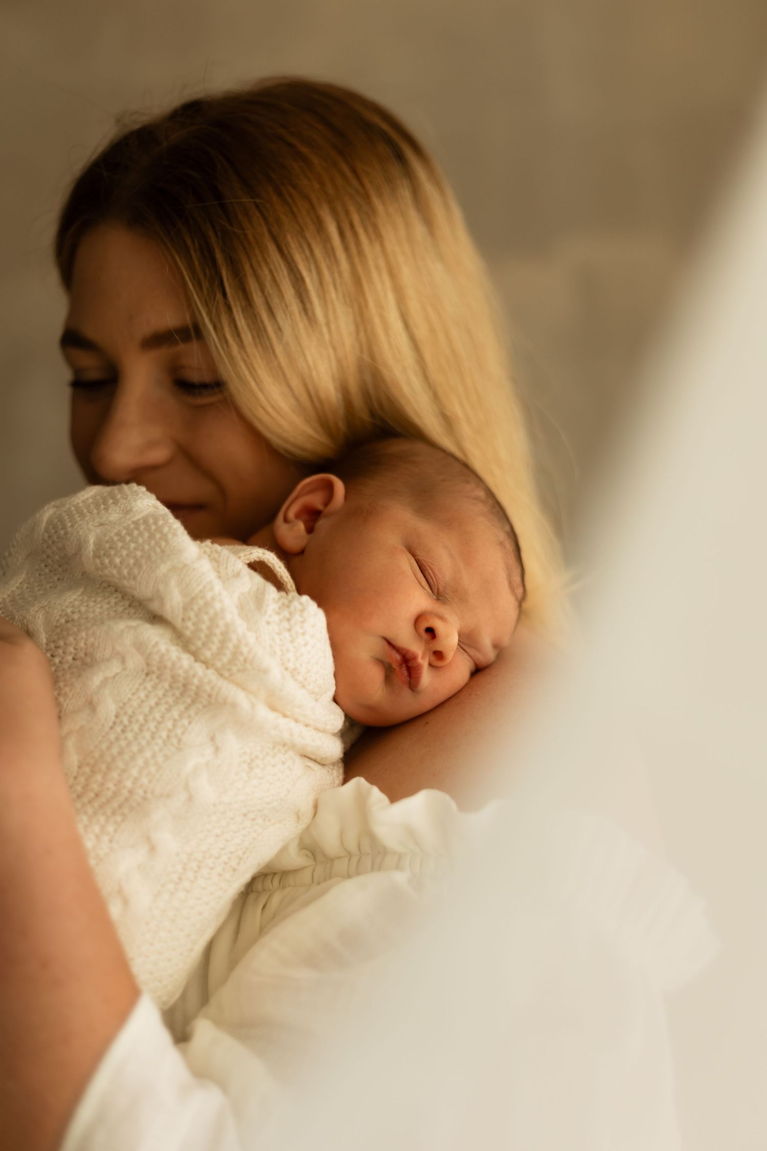 A peaceful moment shows a sleeping baby in a white knit sweater nestled close in warm ambient lighting.
