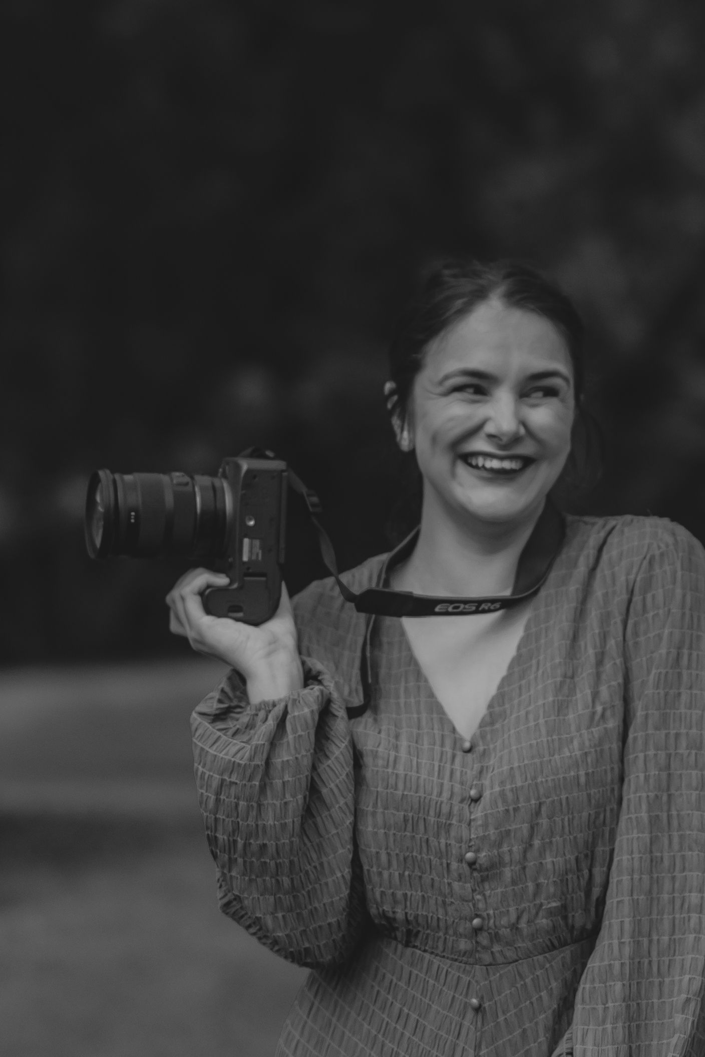 Photographer holding a vintage camera wearing a textured button-up dress captured in black and white.