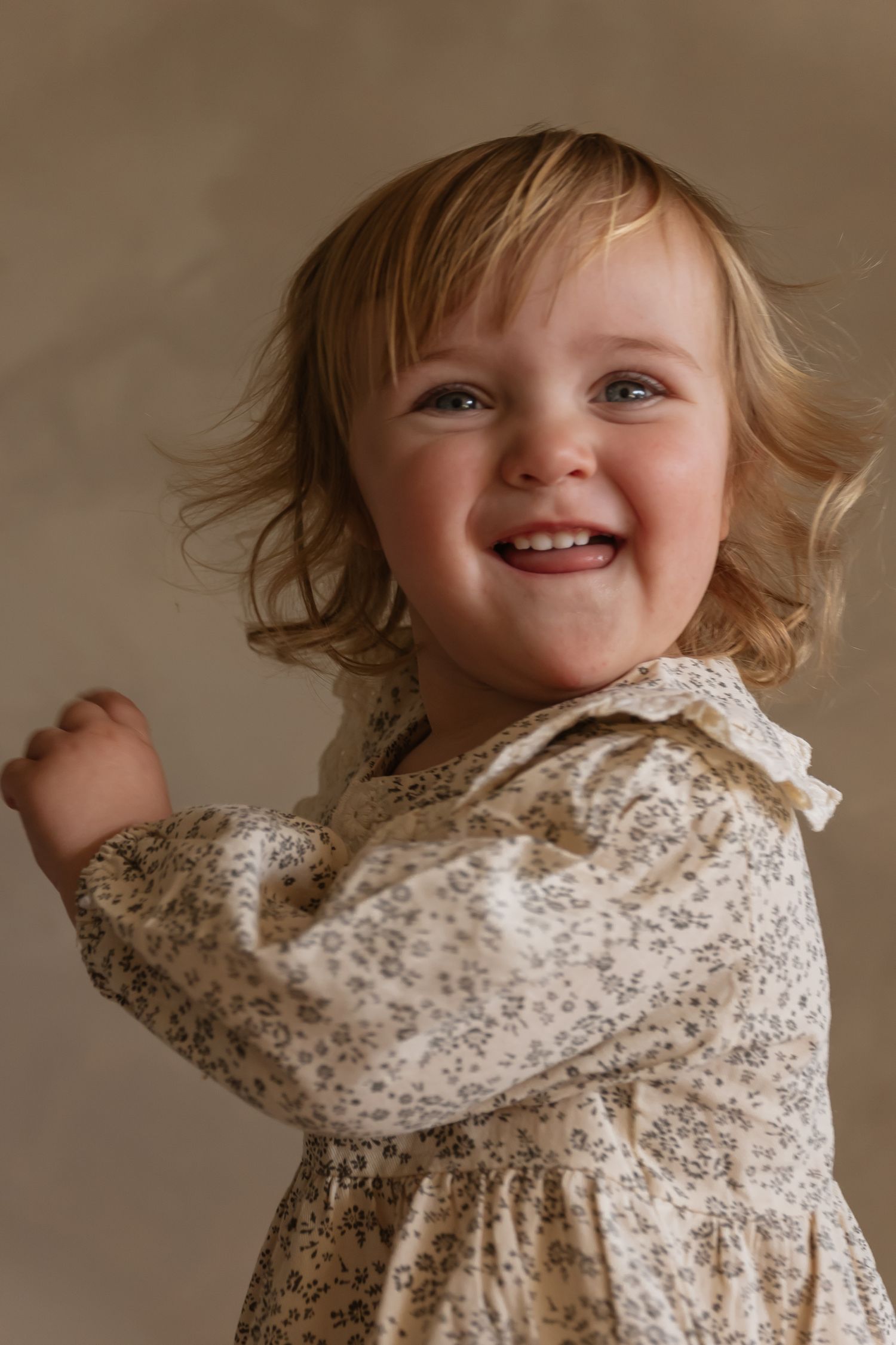 A joyful small child wearing a floral dress smiles brightly against a neutral background.